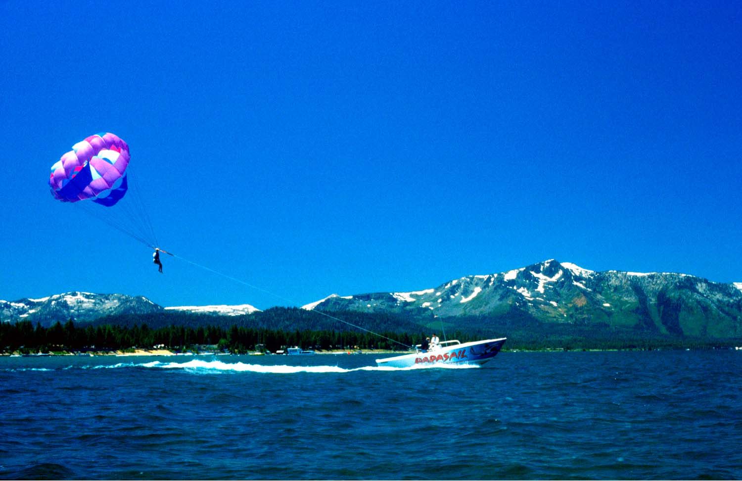 Parasailer towed behind a boat on Lake Tahoe with snowy mountains behind